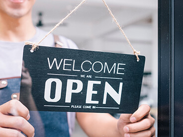 One person turns over a sign that says "Welcome, we are open".