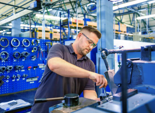 A man wearing glasses is repairing a Lenze component in a factory with a tool rack in the background.