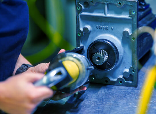 Close-up of a person holding a metal gear and a round component on a workbench.